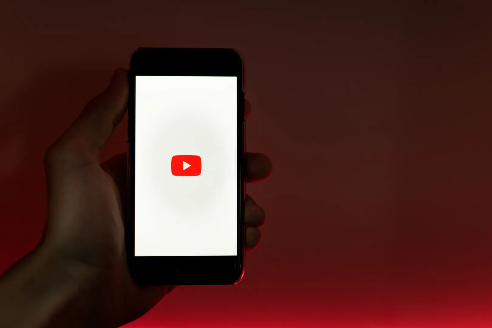 A hand holding a smartphone while the YouTube app opens.