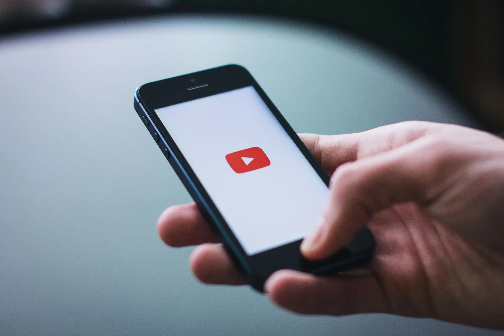 Person holding a mobile phone with the YouTube logo displayed on screen.